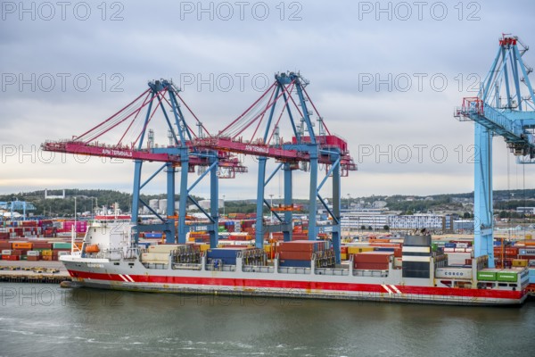 Large port with several blue and red cranes and container ships under cloudy sky, Gothenburg,
