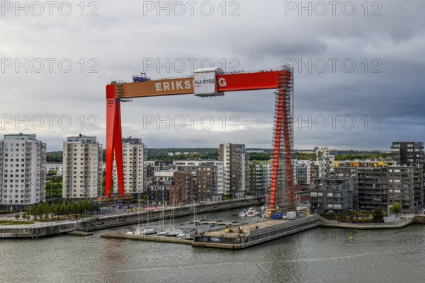 Large orange construction crane in front of modern residential buildings on the site of the former