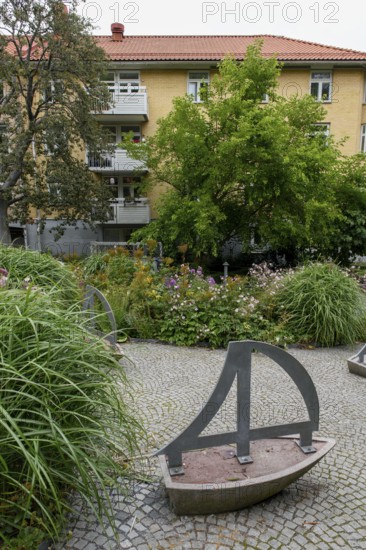 Green garden with art installations and lush plants in front of a residential building, Gothenburg,