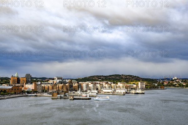 Urban landscape with waterside buildings and hills in the background under cloudy sky, Gothenburg