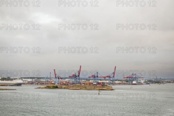 View of container bridges in Gothenburg harbour with cranes and water in the foreground under grey