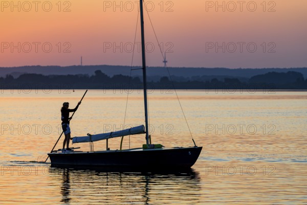 Sailing boat with person on calm Dümmer See brought into the harbor with a long stake at sunset,