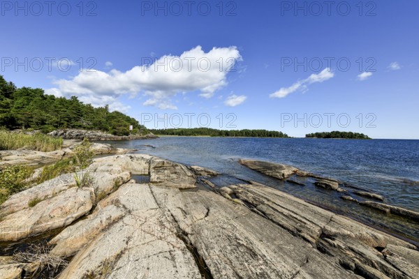 Clear sky over rocky archipelago coastline with granite archipelago with green forest and blue
