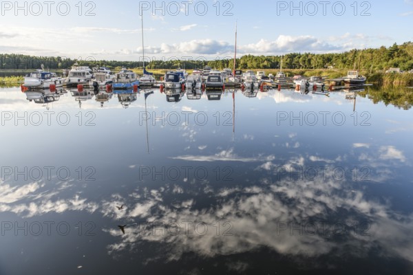 Several boats are moored in the quiet sports boat harbor of Ekenäs, water reflects the sky and the