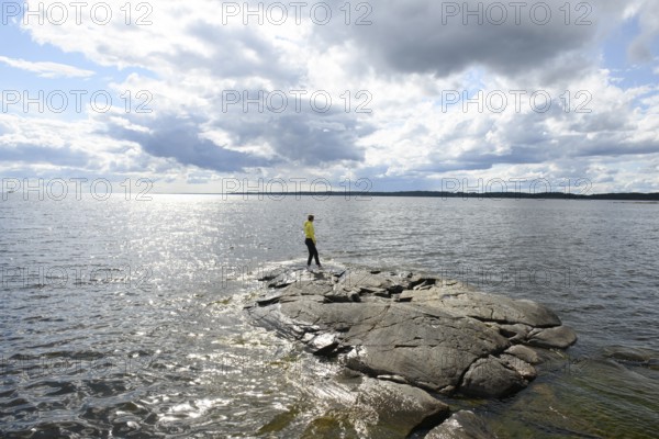 Young woman girl standing on archipelago on rocks at Lake Vänern under cloudy sky, Värmlands län,