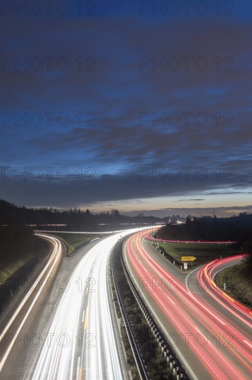 Night view of a motorway with red and white light trails against a cloudy sky, near Stuttgart,