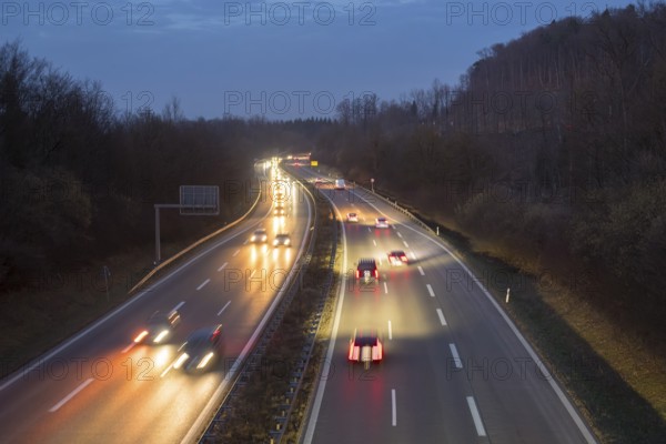 Illuminated motorway in the dark with passing cars, surrounded by hills and trees, near Stuttgart,