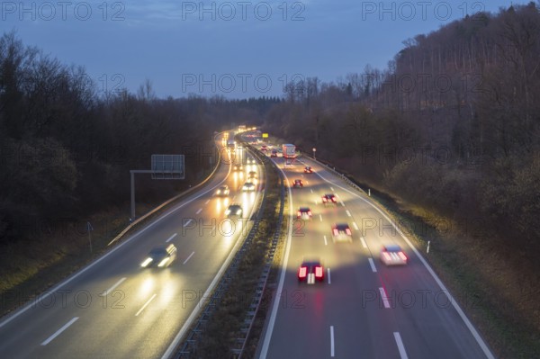 Cars move at night on an illuminated highway, surrounded by trees and darkness, near Stuttgart,