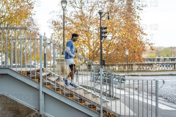 Energetic black man maintaining fitness by running down concrete stairs in an urban setting with