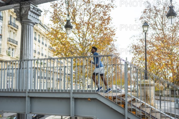 Young man in sportswear running up a metal staircase on a bridge in paris, showing active city