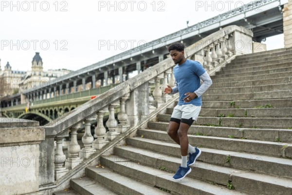 Young black man performing urban jogging and fitness training, actively descending large stone