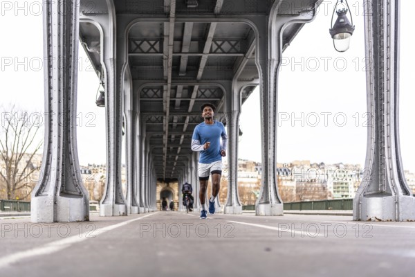 Young man jogging across bir hakeim bridge in paris, energetic urban workout against metal