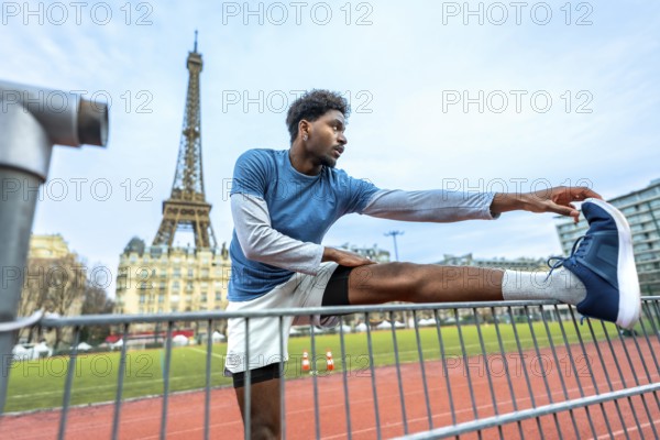 Young athletic man performing stretching exercises on a running track with the iconic eiffel tower