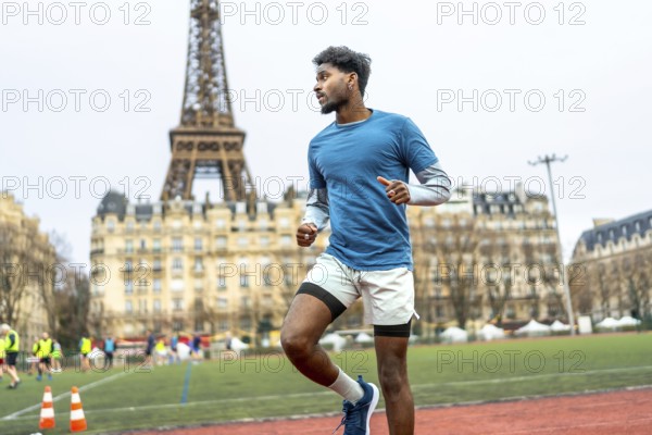 Young black man sprinting and training on an outdoor stadium track with the eiffel tower and