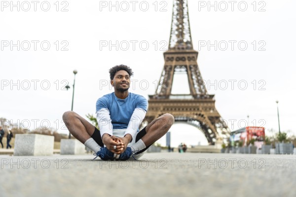 Young black man doing a butterfly stretch on paris pavement, warming up for urban run with the