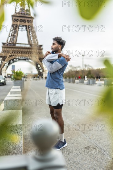 Young athletic man stretching his arms and shoulders on a city street in paris, preparing for an