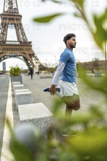 Young athletic man in sportswear stretching his quadriceps on a paris street with the eiffel tower