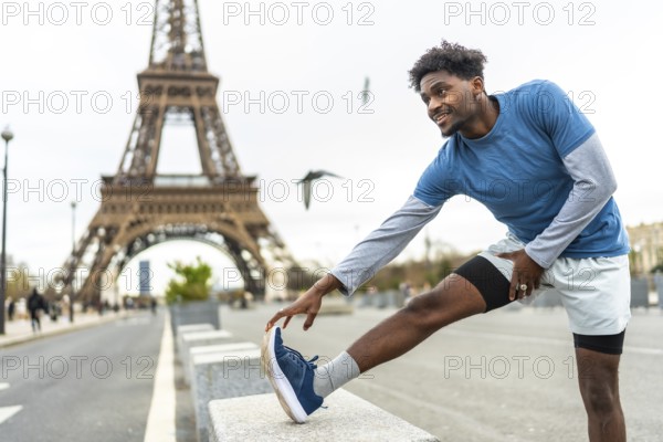 Young black man stretching leg on a concrete barrier with the eiffel tower in the blurred