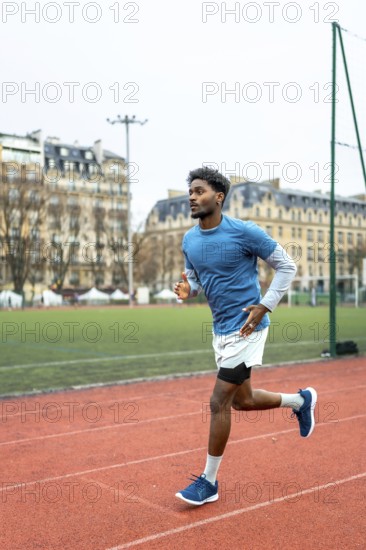 Male athlete with dark skin running on an urban athletic track, training for endurance and