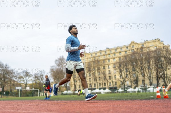 Young man training on a paris stadium running track, jogging in sportswear with focused