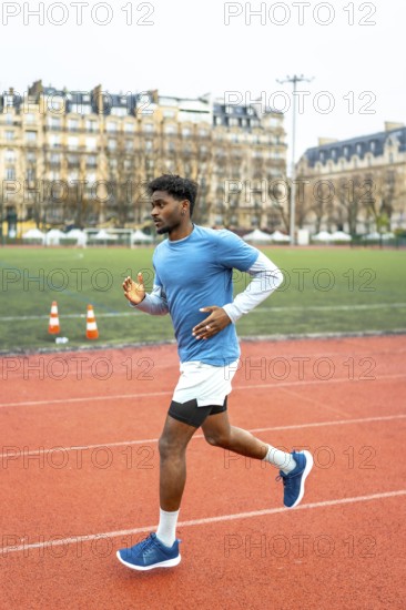 Young dark skinned athlete sprinting on a red urban track in paris, full body side view capturing