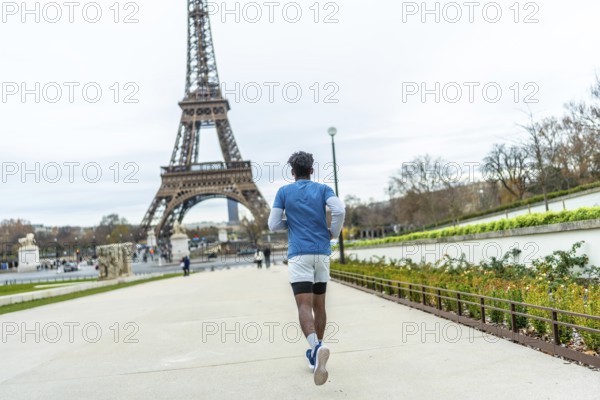 Young man in athletic wear jogging through a park pathway with the iconic eiffel tower prominently