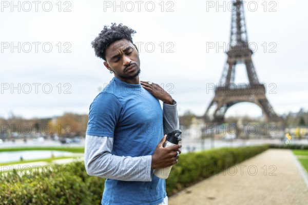 Young black athlete feeling neck pain and fatigue after exercising in a park, holding a water