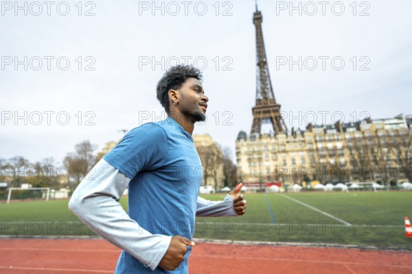 Young black man with curly hair running on a red athletic track in the city, the iconic eiffel