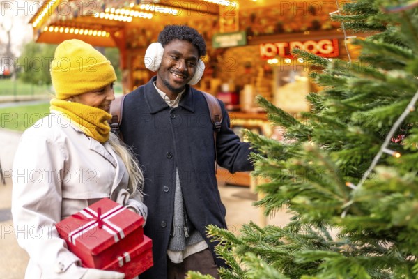 Joyful multiethnic couple holding red gifts, smiling as they stroll a festive paris christmas