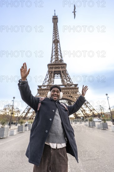 Young man with winter earmuffs raising arms in excitement and smiling widely while visiting the