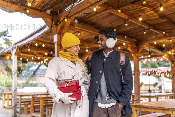 Diverse couple walking together and exchanging smiles in a festive outdoor christmas market in