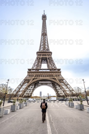 Solo traveler with backpack walks down a paris street toward the iconic eiffel tower, contemplating