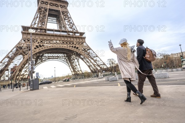 Happy couple holding hands and pointing toward the iconic eiffel tower while walking paris streets