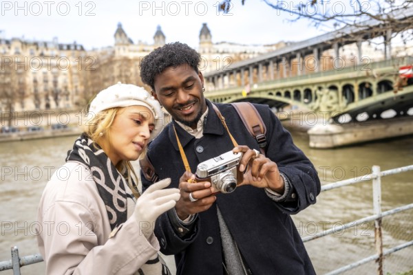 Young multiracial travelers enjoying a romantic city trip to paris, standing by the seine river and
