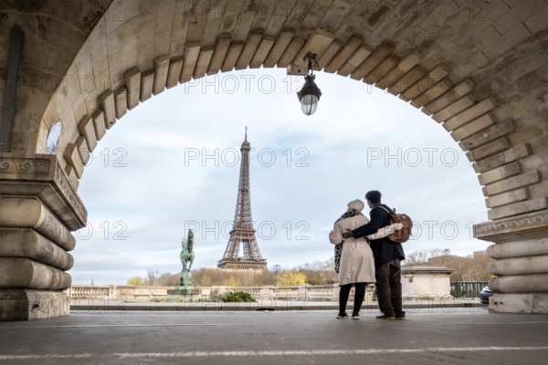 Couple stands embraced on pont de bir hakeim, framed by an ancient archway, observing the eiffel