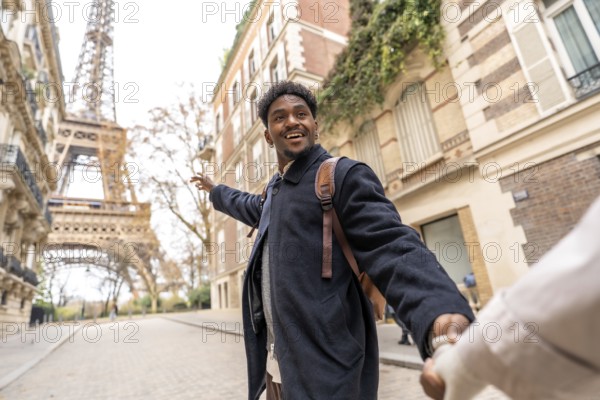 Happy young man of african descent leads his partner by the hand, pointing toward the eiffel tower