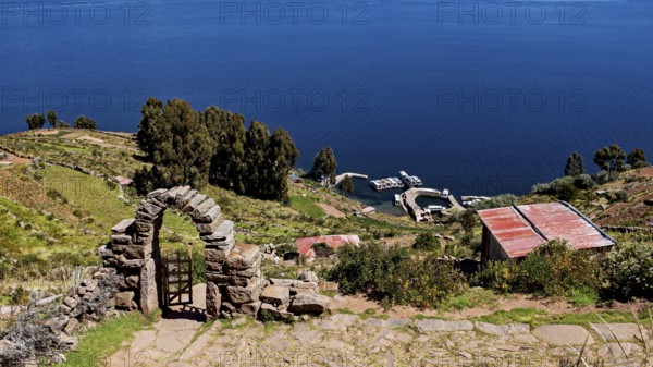 Stone archway with a view of the lake and shore. Surrounded by green hills and clear blue water,