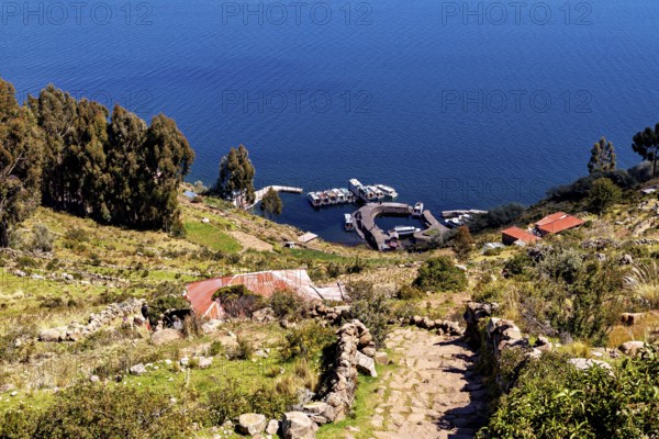 Trail leads to boats on the shores of a deep blue lake surrounded by vegetation, countryside and