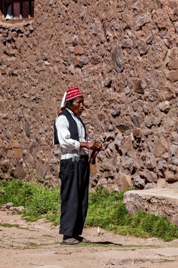 Elderly man wearing traditional clothes next to a stone wall under clear skies, The knitting men on