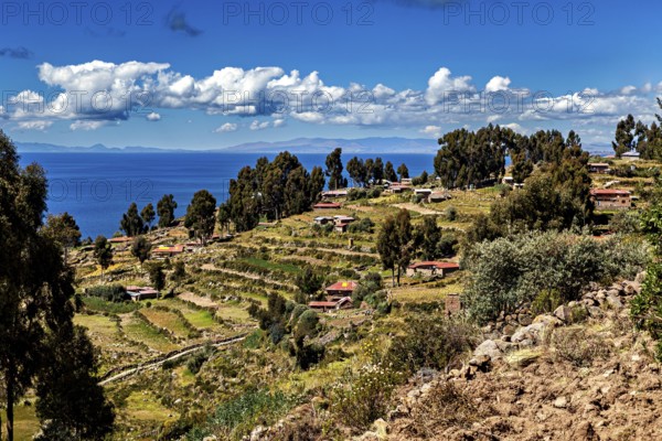 A terraced village stretches along a hill overlooking a blue lake, countryside and farmhouses on