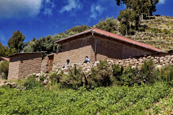 Two people in front of rustic farm houses surrounded by green fields under a blue sky, the