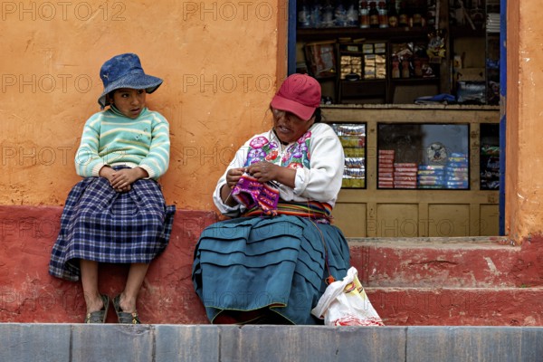 Two woman in traditional clothes sit on a staircase next to a small shop, The woman on Taquile