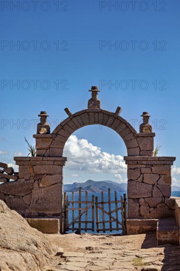 A stone archway with decorations that opens up to a vast mountain panorama under a blue sky, stone