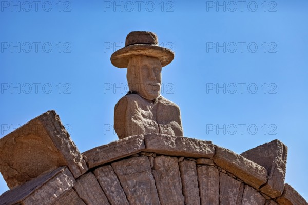 Stone bust with hat on an archway, artfully designed against a clear blue sky, stone gates on the