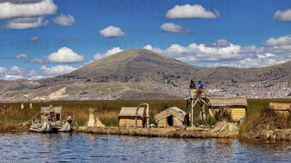 Reed huts and lakeside observation tower with mountains in the background under blue sky, The