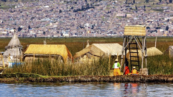 Small village of reed huts with people on the shore in front of an extensive urban landscape, The