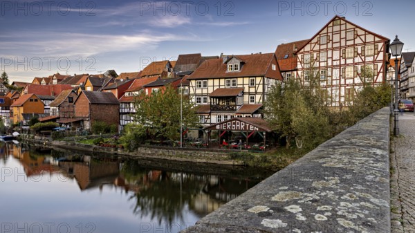 Historic half-timbered houses and beer garden along a river with a bridge at dusk, The town of Bad
