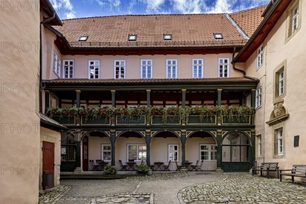 A quiet courtyard with historic half-timbered elements, balconies and decorative flowers under a