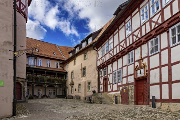 A picturesque courtyard with half-timbered buildings, red tile roofs and a clear blue sky, The