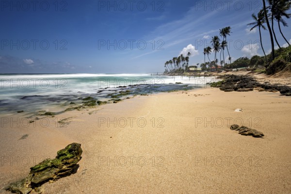 Sunny Kauam beach with palm trees, endless ocean, rocks and waves under a blue sky, Koggala beach